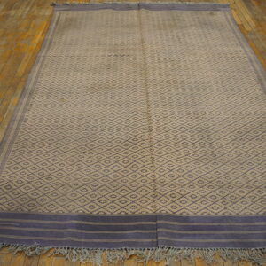 Large beige flatweave rug with dark blue diamond pattern and striped ends on wood flooring.