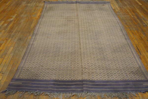 Large beige flatweave rug with dark blue diamond pattern and striped ends on wood flooring.