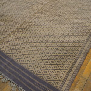 Low pile rug with tan and indigo diamond pattern, striped border, and fringe on distressed wood.