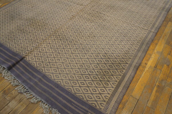 Low pile rug with tan and indigo diamond pattern, striped border, and fringe on distressed wood.