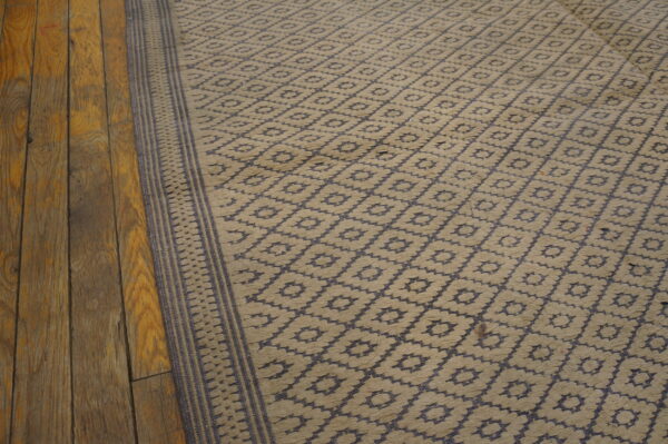 Textured tan and blue geometric rug with a striped border lying on rustic hardwood planks.