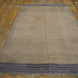Flatweave runner featuring a beige and gray-blue diamond pattern resting on distressed wood flooring.