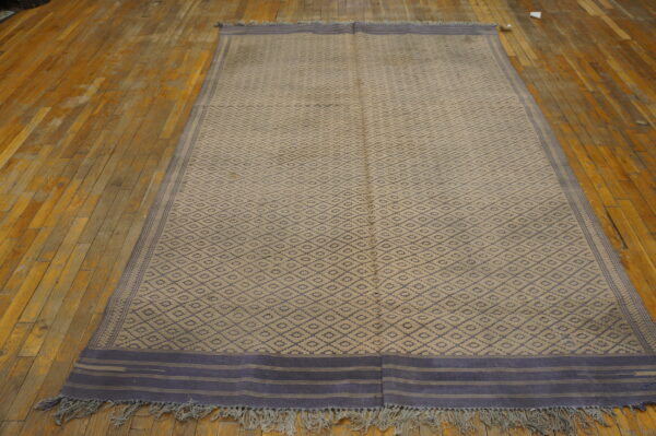 Flatweave runner featuring a beige and gray-blue diamond pattern resting on distressed wood flooring.