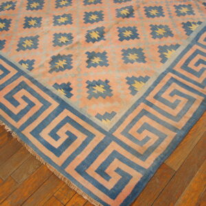 Salmon and blue geometric rug with a Greek key border and star motifs sits on an orange hardwood floor.