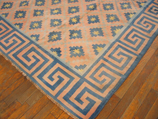 Salmon and blue geometric rug with a greek key border and star motifs sits on an orange hardwood floor.