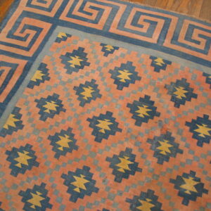 Coral, navy, and yellow flat-weave rug with a meander border and geometric star motifs on wood planks.