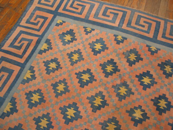 Coral, navy, and yellow flat-weave rug with a meander border and geometric star motifs on wood planks.