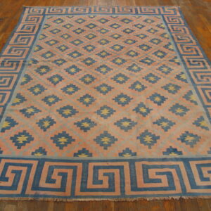 Coral, blue, and yellow flatweave rug with a meander border and geometric pattern on wood flooring.