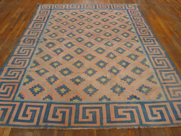 Coral, blue, and yellow flatweave rug with a meander border and geometric pattern on wood flooring.