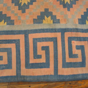 Geometric flatweave rug in blue, pink, and yellow with a meander border over wood flooring.