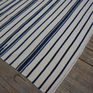 White and navy flatweave rug with vertical stripes lying on distressed gray wood flooring.