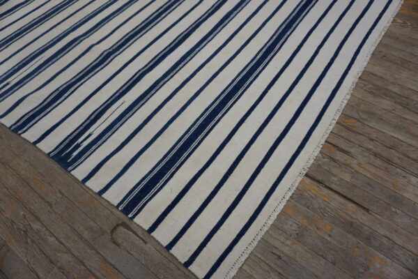 White and navy flatweave rug with vertical stripes lying on distressed gray wood flooring.
