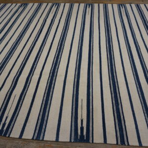 A large cream and navy flatweave rug with vertical stripes covers rustic wood flooring.