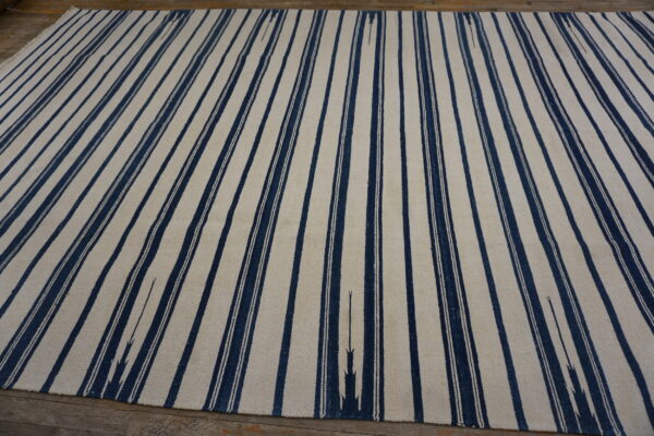 A large cream and navy flatweave rug with vertical stripes covers rustic wood flooring.