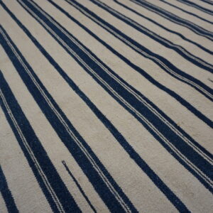 A flatwoven rug featuring wide vertical stripes in off-white alternating with narrow dark blue stripes.
