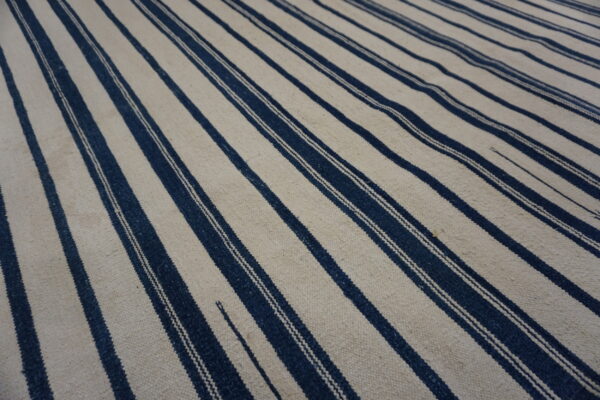 A flatwoven rug featuring wide vertical stripes in off-white alternating with narrow dark blue stripes.