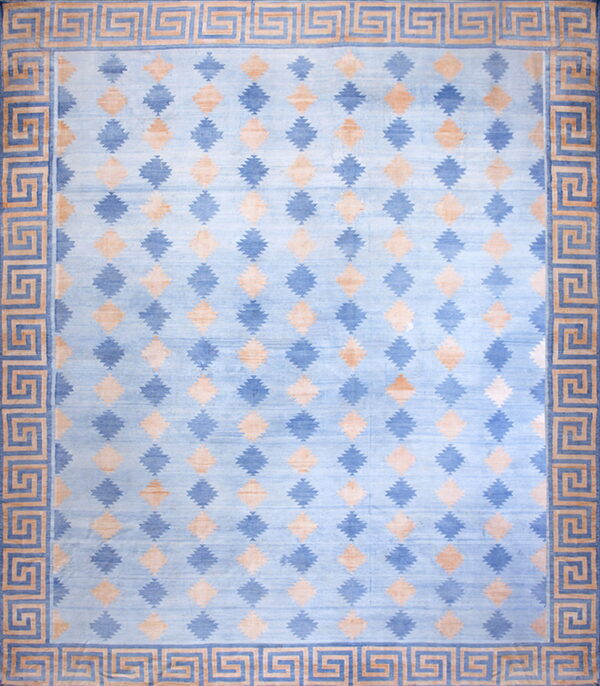 A blue and tan rug with repeating lozenge shapes and a thick greek key border.