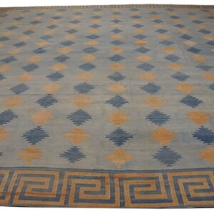 Blue rug with geometric serrated diamonds and a tan and dark blue Greek key border.
