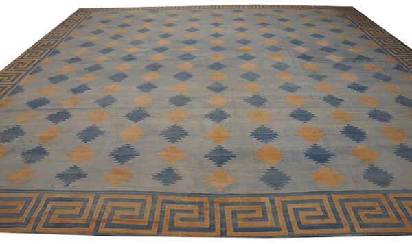 Blue rug with geometric serrated diamonds and a tan and dark blue greek key border.