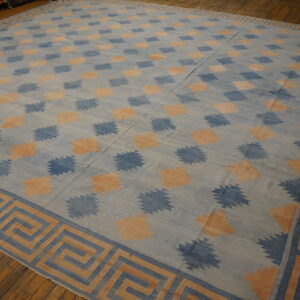 Large blue and peach flatweave rug with geometric patterns and a Greek key border on wood floors.