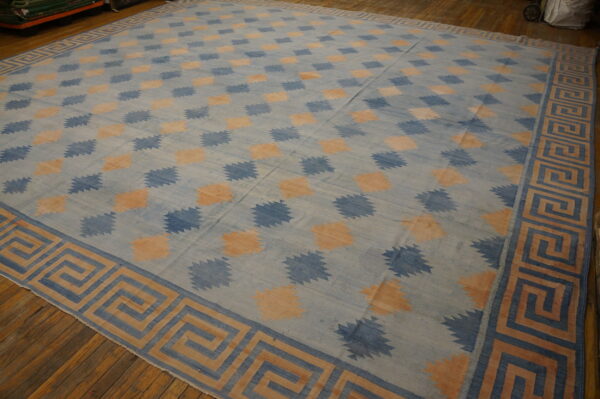 Large blue and peach flatweave rug with geometric patterns and a greek key border on wood floors.