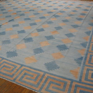 Blue and peach flatweave rug with repeating jagged diamond motifs and a wide meander border on a wood floor.