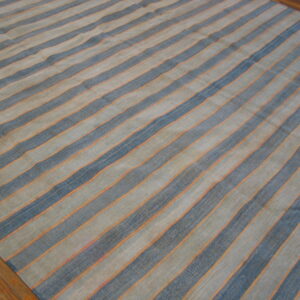 A low-pile striped rug in slate blue, muted tan, and thin orange lines rests on a wood floor.
