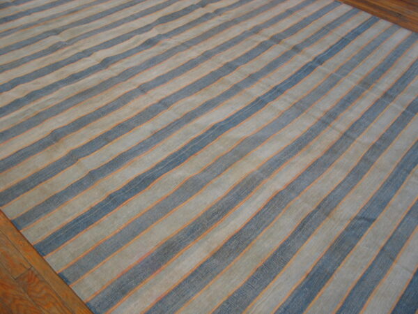 A low-pile striped rug in slate blue, muted tan, and thin orange lines rests on a wood floor.