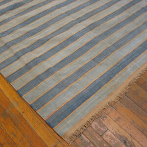 Low-pile rug with alternating blue and tan stripes separated by thin orange lines rests on a wood floor.
