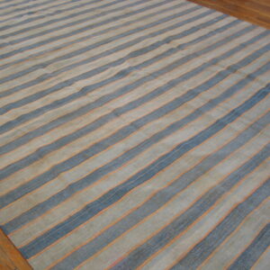 Low-pile rug with wavy blue and tan stripes separated by thin orange lines on wood flooring.