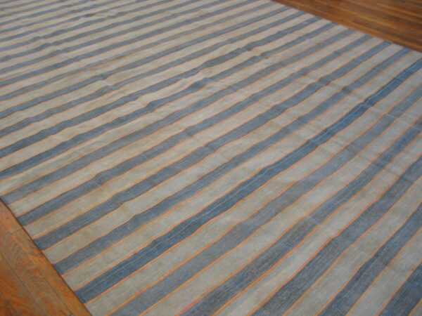 Low-pile rug with wavy blue and tan stripes separated by thin orange lines on wood flooring.