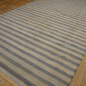 Flatwoven rug featuring light blue and dark blue stripes accented by thin orange lines on wood planks.