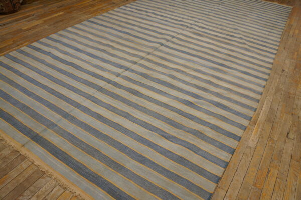Flatwoven rug featuring light blue and dark blue stripes accented by thin orange lines on wood planks.