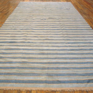 Blue and gray striped flatweave rug with thin orange accents lies on glossy wooden planks.