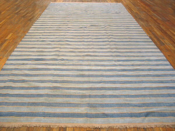 Blue and gray striped flatweave rug with thin orange accents lies on glossy wooden planks.