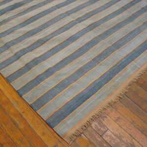 Flatweave rug with wide blue and gray stripes bordered by thin orange lines on wood floor.