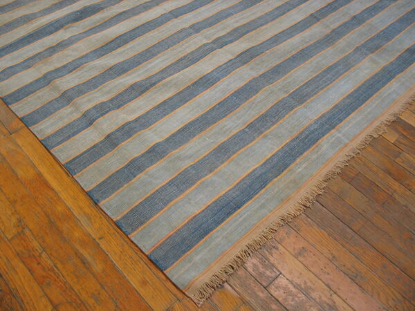 Flatweave rug with wide blue and gray stripes bordered by thin orange lines on wood floor.