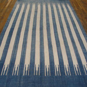 Blue and cream striped rug featuring abstract pronged motifs laid on a brown hardwood floor.