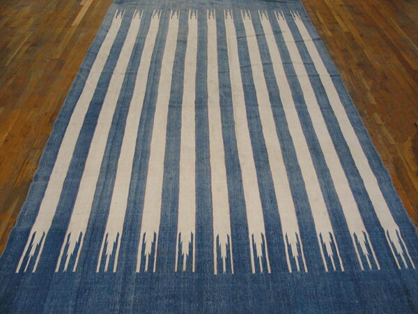 Blue and cream striped rug featuring abstract pronged motifs laid on a brown hardwood floor.