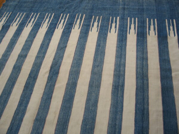Textured blue and cream flatweave rug with vertical stripes featuring jagged geometric terminations at the top edge.