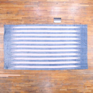 Blue and white striped flat-woven rug with ikat edges on distressed plank hardwood flooring.