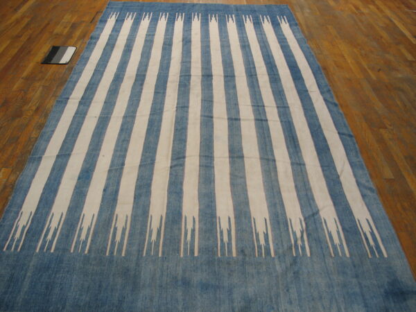Low-pile rug with wide blue and cream vertical stripes, featuring stylized jagged ends on wood floor.