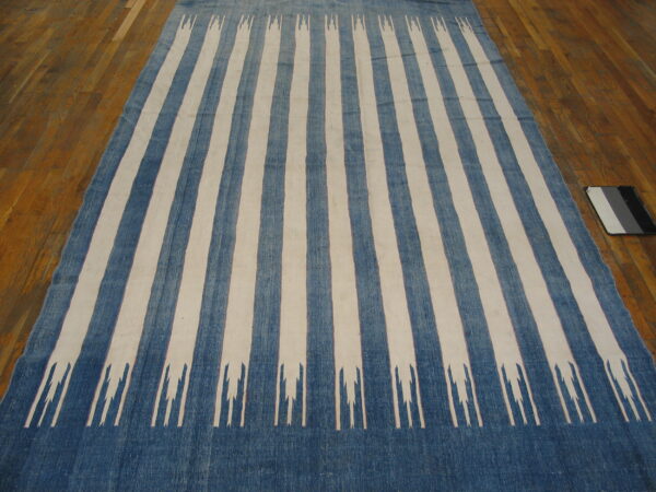 A low-pile blue and cream striped rug with jagged white motifs is displayed on a wood plank floor.