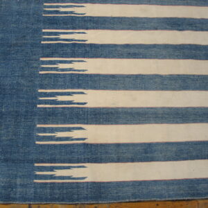 Textured blue and off-white rug with horizontal stripes and jagged edges rests on a wood floor.