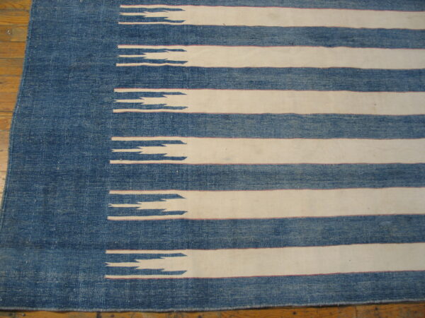 Textured blue and off-white rug with horizontal stripes and jagged edges rests on a wood floor.