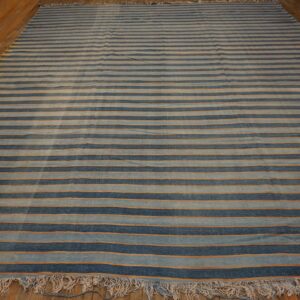 Striped rug featuring wide navy and light blue bands with thin orange lines on wood flooring.