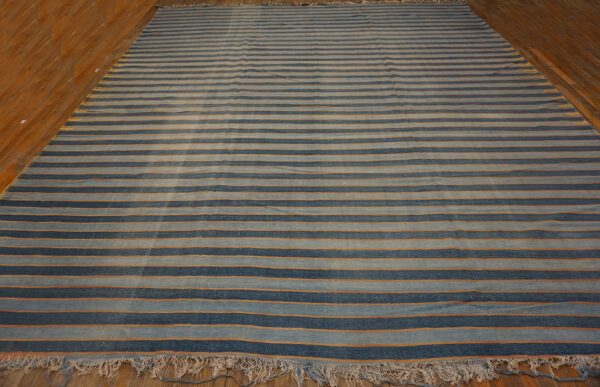 Striped rug featuring wide navy and light blue bands with thin orange lines on wood flooring.