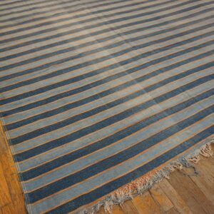 Blue and light blue striped rug with thin orange lines rests on a distressed wood floor.