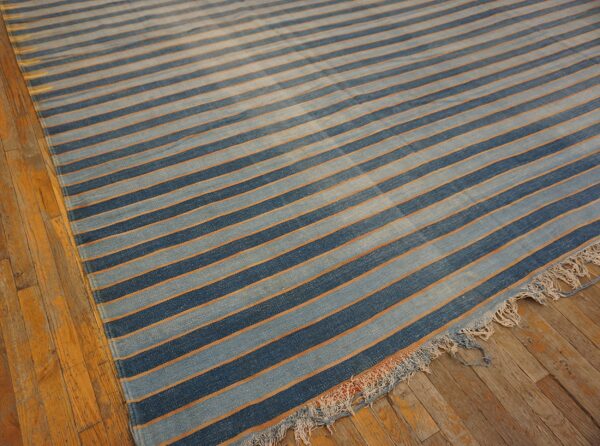 Blue and light blue striped rug with thin orange lines rests on a distressed wood floor.