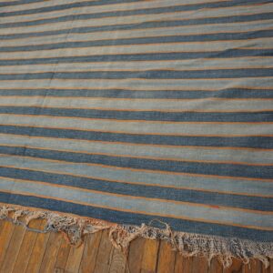 A flatweave rug featuring wide blue stripes and thin orange lines is displayed on rustic wood floors.